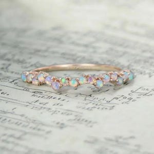 Puede incluir: Un delicado anillo de banda de oro rosa con una fila curva de piedras de ópalo iridiscentes.