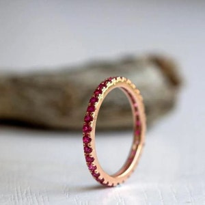 Puede incluir: Un delicado anillo de banda de oro con una fila de eternidad completa de pequeñas piedras de rubí rojo brillante.