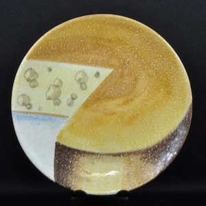 May include: A round ceramic plate with a cheese design. The plate features a wedge of cheese with holes, and the rest of the plate is a yellow-brown color. The bottom edge is a dark brown color.