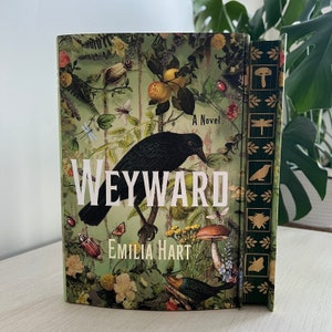 May include: A green, brown, and black book cover with a black crow, flowers, and the title "WEYWARD" in white letters. The book is titled "A Novel" and the author is "EMILIA HART".