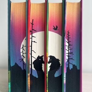 Könnte beinhalten: Fünf Buchrücken mit einem Farbverlauf von Rosa, Orange, Gelb und Lila. Die Rücken sind mit einer Silhouette von zwei Wölfen verziert, die zum Vollmond heulen, Bäumen und einem Vogel, der über ihnen fliegt.