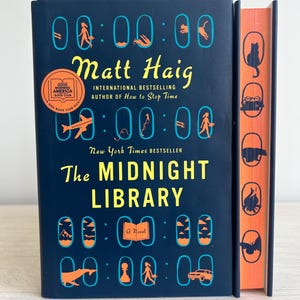 Può includere: Un libro rilegato in blu con il titolo "The Midnight Library" di Matt Haig. Il libro è un best-seller del New York Times e una scelta del Good Morning America Book Club. La copertina presenta una serie di orologi con diversi simboli all'interno di ogni orologio.
