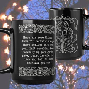 May include: Two black ceramic mugs with white floral designs and text. The text on one mug reads, "There are some things I know for certain: always throw spilled salt over your left shoulder..." The mugs have black handles.
