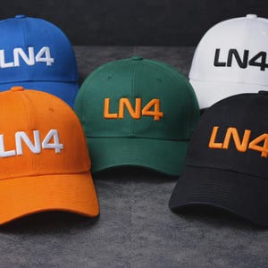 May include: A selection of baseball caps in shades of blue, orange, green, white, and black. Each cap displays the embroidered text "LN4" in a contrasting colour. The caps are made from a sturdy material and have a curved peak.