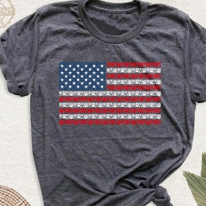 May include: A gray t-shirt with a red, white, and blue American flag design. The flag is made of small white stars on a blue background and red and white stripes. The flag is centered on the shirt.
