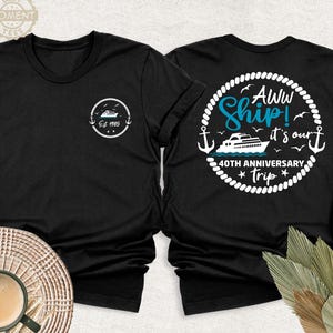 May include: Two black t-shirts with white text and graphics. The left t-shirt has a white circle with a small boat and the text 'Est. 1985'. The right t-shirt has a white circle with a larger boat, the text 'Aww Ship! It's our 40th Anniversary Trip', and a rope design around the circle.