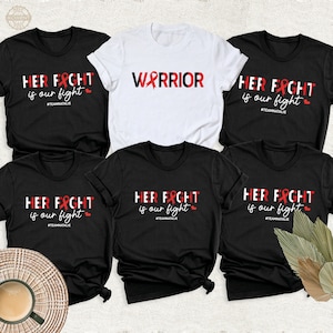 May include: Five t-shirts with different designs. Three black t-shirts with the text "HER FIGHT is our fight #TEAMNATALIE" and a red ribbon. One white t-shirt with the text "WARRIOR" and a red ribbon. One black t-shirt with the text "HER FIGHT is our fight #TEAMNATALIE" and a red ribbon.