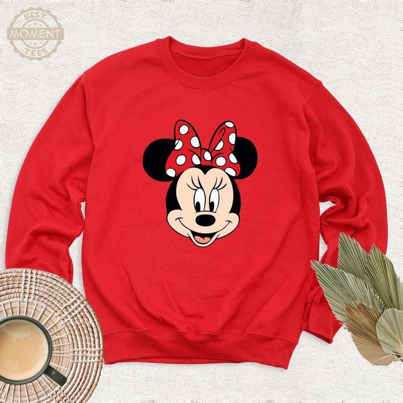 May include: Red sweatshirt with a white and red Minnie Mouse graphic. Minnie Mouse is wearing a red bow with white polka dots.
