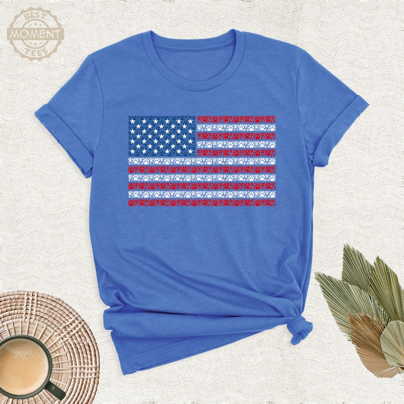 May include: A royal blue t-shirt with a red, white, and blue American flag design. The flag is made up of paw prints.