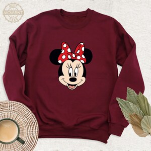 Peut inclure: Un sweat-shirt bordeaux avec une image de dessin anim&eacute; de Minnie Mouse portant un n&oelig;ud rouge &agrave; pois blancs.