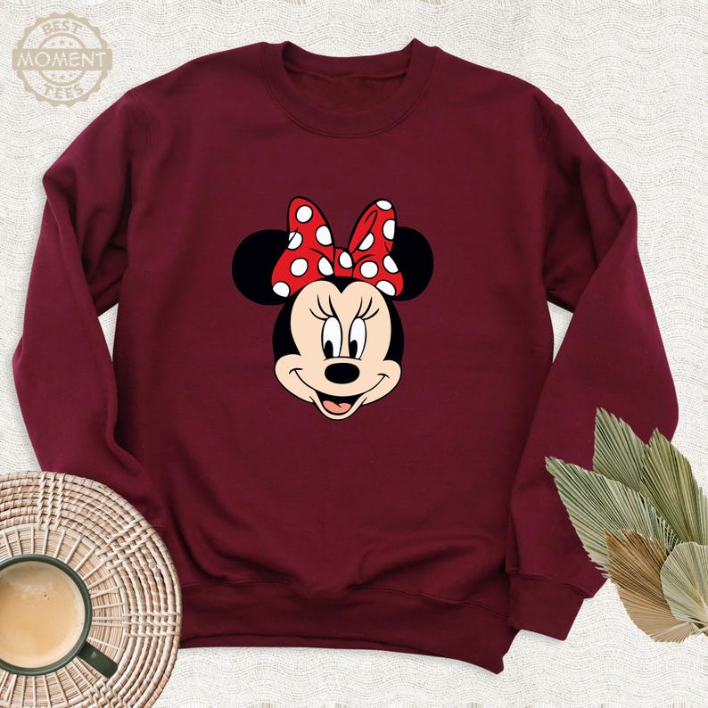 Peut inclure: Un sweat-shirt bordeaux avec une image de dessin anim&eacute; de Minnie Mouse portant un n&oelig;ud rouge &agrave; pois blancs.