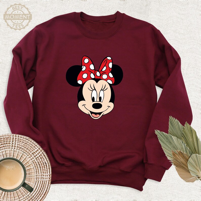 Peut inclure: Un sweat-shirt bordeaux avec une image de dessin anim&eacute; de Minnie Mouse portant un n&oelig;ud rouge &agrave; pois blancs.