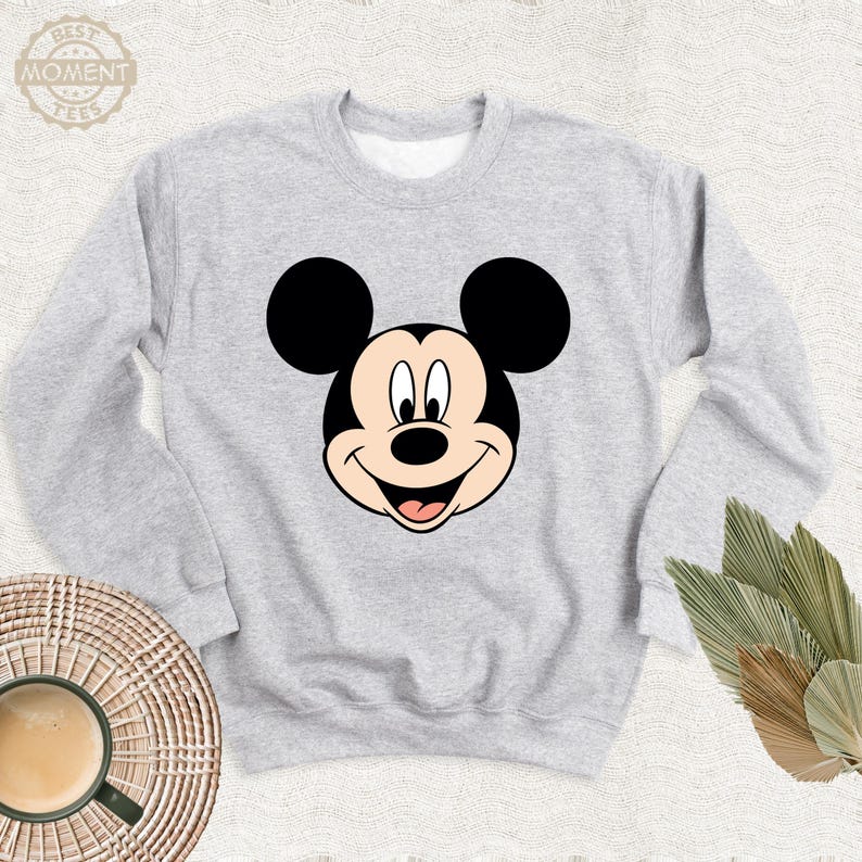 May include: A grey sweatshirt featuring a cartoon image of Mickey Mouse's face on the front.