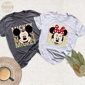 May include: Two gray t-shirts with a vintage-style graphic of Mickey Mouse and Minnie Mouse. The Mickey Mouse shirt has the word "Mickey" repeated in a stacked design. The Minnie Mouse shirt has the word "Minnie" repeated in a stacked design.