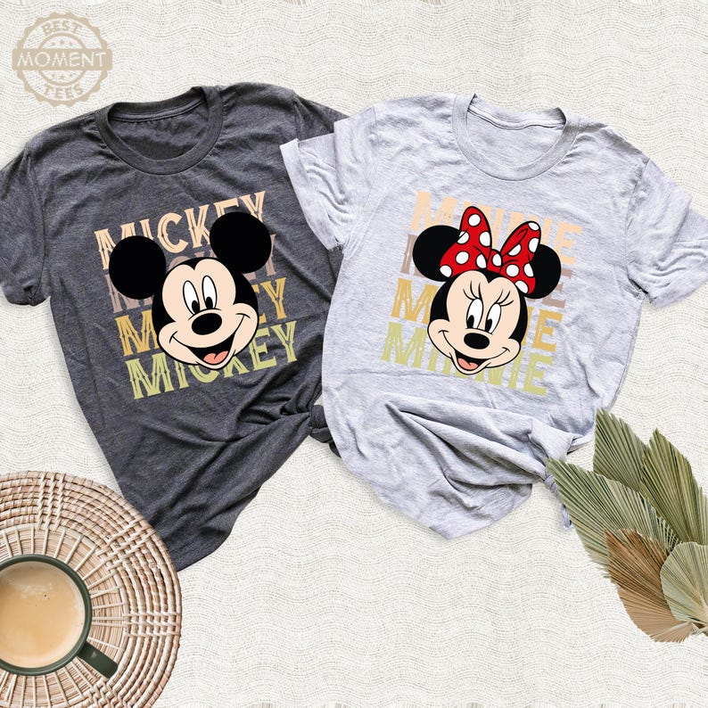 May include: Two gray t-shirts with a vintage-style graphic of Mickey Mouse and Minnie Mouse. The Mickey Mouse shirt has the word "Mickey" repeated in a stacked design. The Minnie Mouse shirt has the word "Minnie" repeated in a stacked design.