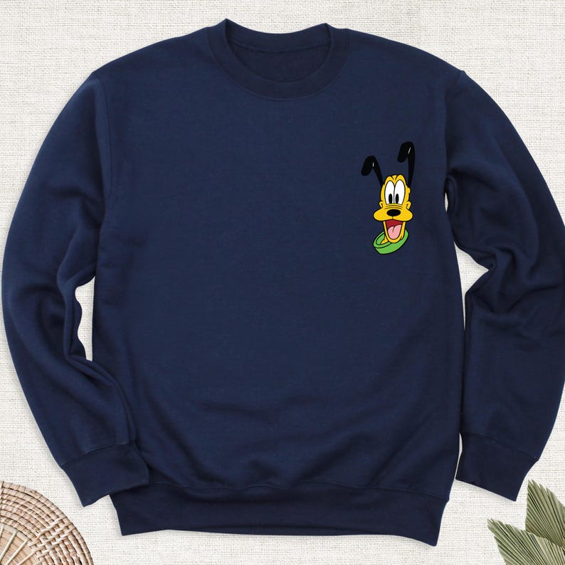 May include: Navy blue sweatshirt featuring a cartoon image of Pluto, the Disney dog, on the upper left chest. The graphic shows Pluto's face with his tongue sticking out, set against a green collar. The sweatshirt has a crew neck and long sleeves.