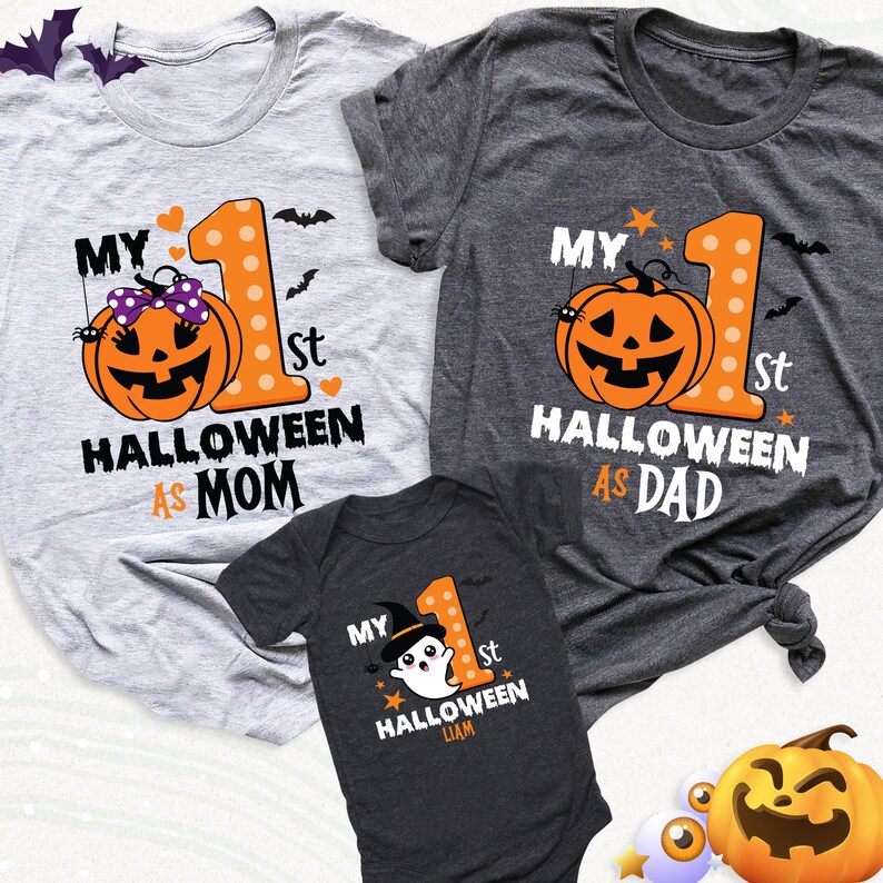 K&ouml;nnte beinhalten: Drei Halloween-Shirts. Zwei T-Shirts f&uuml;r Erwachsene, eines grau und eines dunkelgrau, zeigen eine K&uuml;rbisgrafik und den Text "My 1st Halloween As Mom" und "My 1st Halloween As Dad". Ein dunkelgrauer Baby-Body hat eine Geistergrafik und den Text "My 1st Halloween".