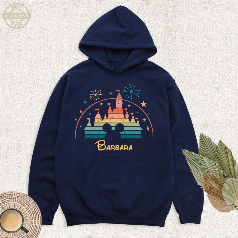 May include: A navy blue hoodie with a vintage-style graphic of a rainbow-colored castle with fireworks and the text "BARBARA" underneath. The castle is a silhouette of the iconic Disney castle.