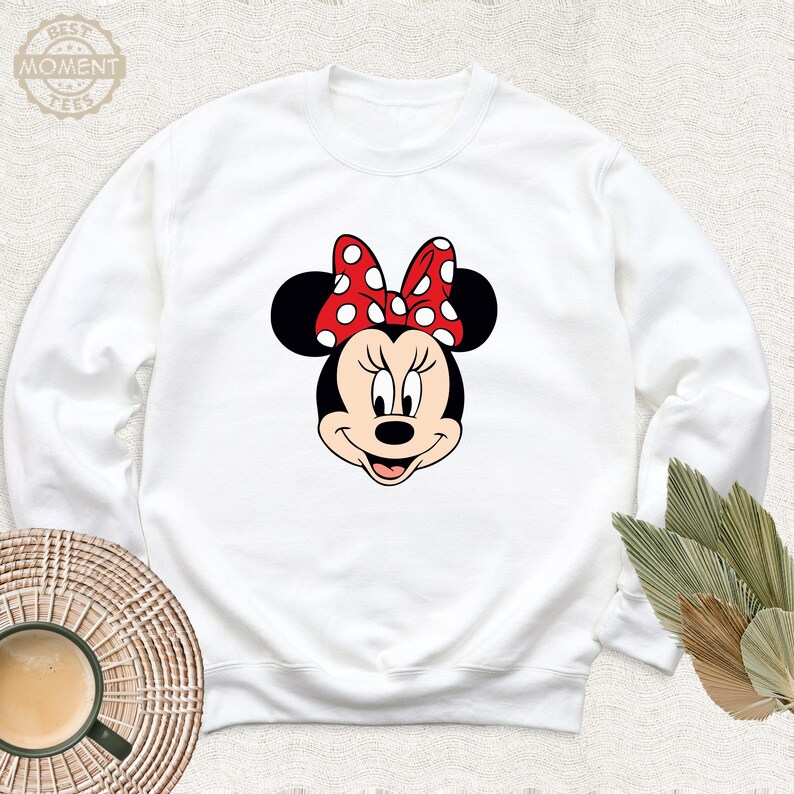 Peut inclure: Sweat-shirt blanc &agrave; manches longues avec une image de dessin anim&eacute; rouge et blanc de Minnie Mouse portant un n&oelig;ud rouge &agrave; pois blancs.
