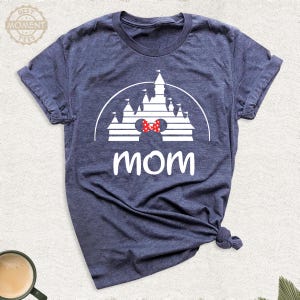 Puede incluir: Camiseta azul marino con un gr&aacute;fico blanco de un castillo, una pajarita roja y la palabra "mam&aacute;" en blanco. La camiseta est&aacute; hecha de un material suave y tiene mangas cortas.