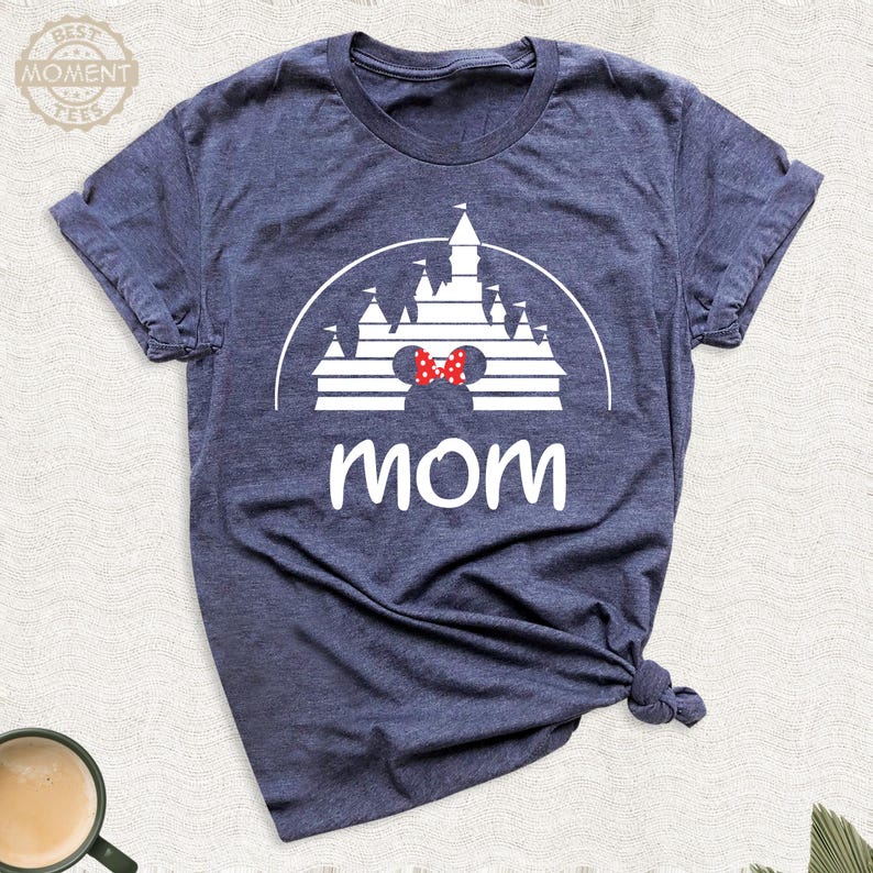 Puede incluir: Camiseta azul marino con un gr&aacute;fico blanco de un castillo, una pajarita roja y la palabra "mam&aacute;" en blanco. La camiseta est&aacute; hecha de un material suave y tiene mangas cortas.
