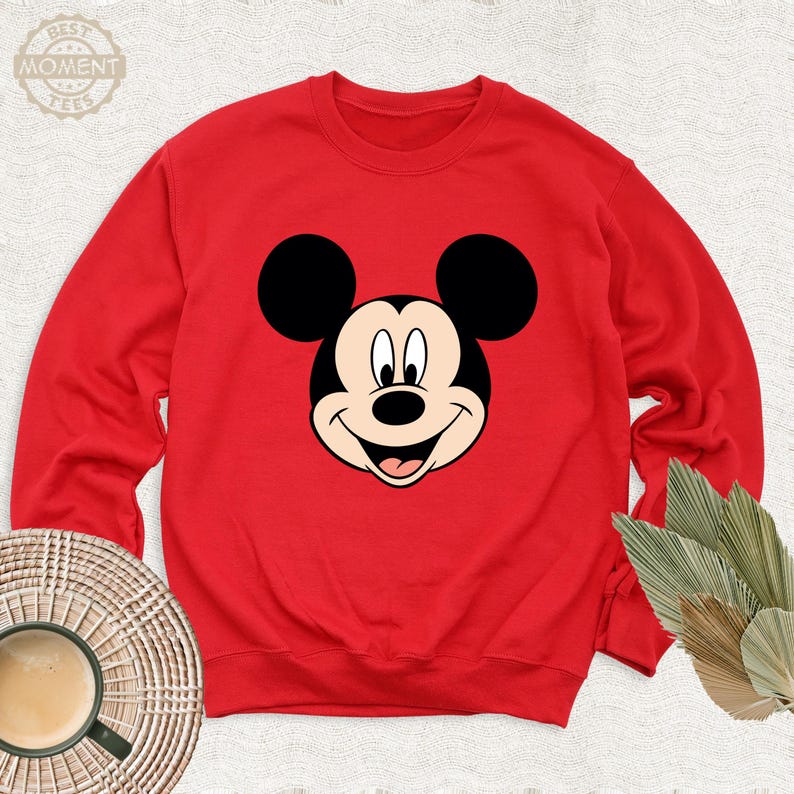 May include: Red sweatshirt featuring a black and white cartoon image of Mickey Mouse on the front.