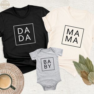 Peut inclure: Un ensemble de trois t-shirts avec les mots "DA DA", "MA MA" et "BABY" imprim&eacute;s en noir sur fond blanc. Les t-shirts sont noir, cr&egrave;me et gris.