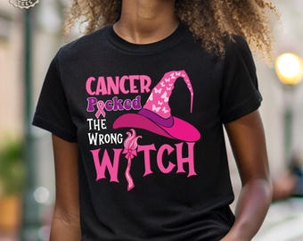 May include: A black short-sleeved t-shirt featuring a pink witch hat with white butterfly patterns and the text "CANCER Picked THE WRONG WITCH" in pink and white lettering, with a pink awareness ribbon replacing the letter C.
