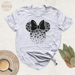 Puede incluir: Camiseta gris claro con un dise&ntilde;o de Minnie Mouse negro hecho de corazones y un lazo. La camiseta tiene mangas cortas y cuello redondo. El texto "BEST MOMENT TEES" est&aacute; en un c&iacute;rculo en la parte superior izquierda.