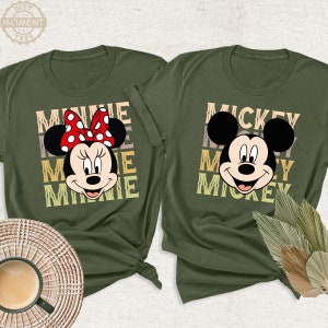 May include: Two green t-shirts with a retro design featuring Mickey Mouse and Minnie Mouse. The Mickey Mouse shirt says "Mickey Mickey Mickey" and the Minnie Mouse shirt says "Minnie Minnie Minnie".