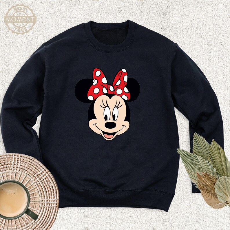Peut inclure: Un sweat-shirt noir avec une image de dessin anim&eacute; rouge et blanc de Minnie Mouse. Minnie Mouse porte un n&oelig;ud rouge &agrave; pois blancs.