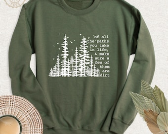 May include: An olive green crewneck sweatshirt featuring a white graphic of a forest silhouette and the text: of all the paths you take in life, make sure a few of them are dirt. The design includes small birds flying above the pine trees.