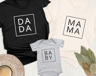 May include: A black t-shirt with the text DADA in a white square, a cream t-shirt with the text MAMA in a black square, and a gray baby bodysuit with the text BABY in a black square, all featuring simple sans-serif typography.