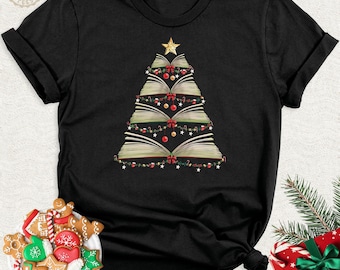 May include: A black short-sleeve t-shirt featuring a graphic of a Christmas tree constructed from stacked open books. The tree is decorated with red ornaments, green garlands, and a gold star at the top. The design is centered on the chest.