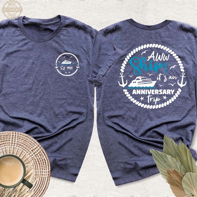 May include: Two navy blue t-shirts with white text and graphics. One shirt says "Aww Ship! It's an Anniversary Trip" with a white anchor and a blue ship. The other shirt says "Est 1985" with a blue ship.