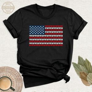 May include: A black t-shirt with a red, white, and blue American flag design. The flag is made up of paw prints.