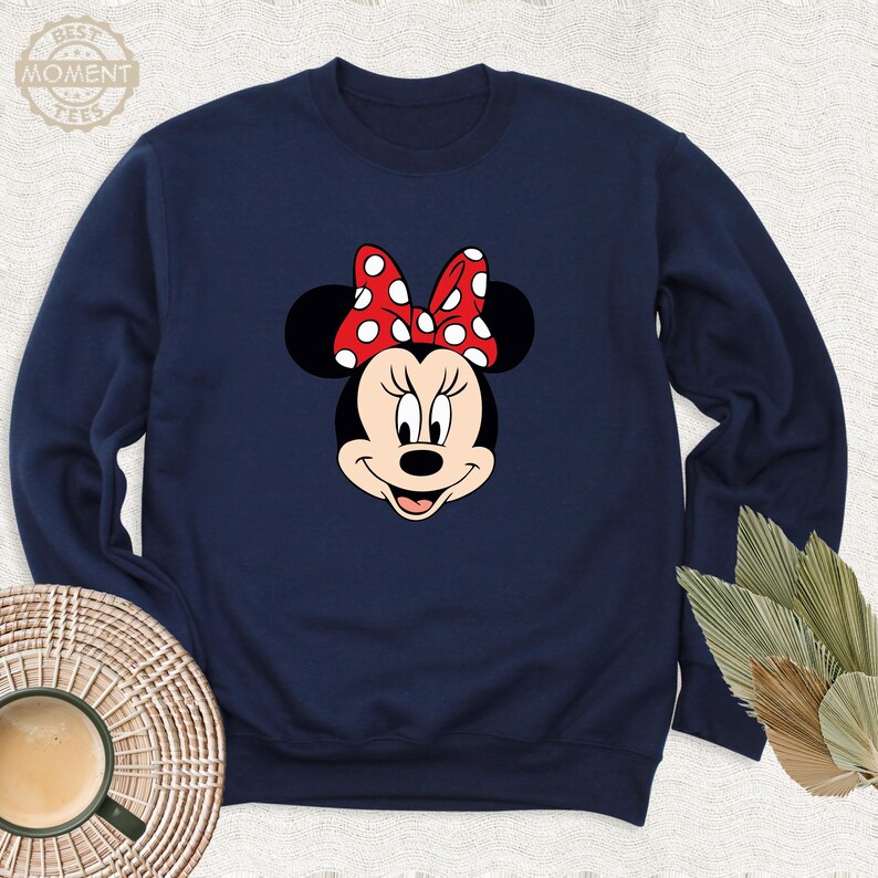 Peut inclure: Un sweat-shirt bleu marine avec une image de dessin anim&eacute; de Minnie Mouse portant un n&oelig;ud rouge &agrave; pois blancs.