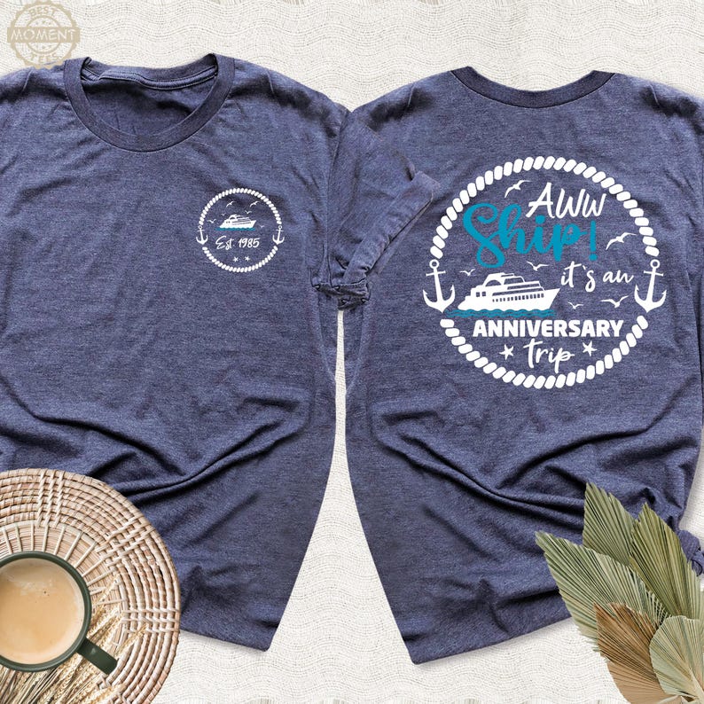 May include: Two navy blue t-shirts with white text and graphics. One shirt says "Aww Ship! It's an Anniversary Trip" with a white anchor and a blue ship. The other shirt says "Est 1985" with a blue ship.