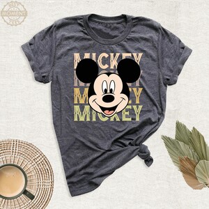 May include: A dark gray t-shirt with a retro-style graphic of Mickey Mouse's face and the word "Mickey" repeated three times in different colors.