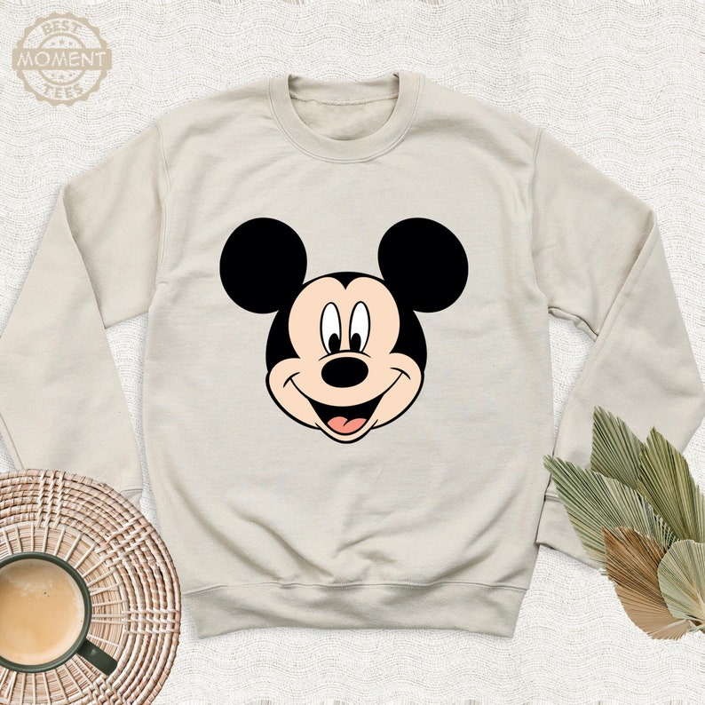 May include: A beige sweatshirt with a black and white Mickey Mouse face graphic on the front.