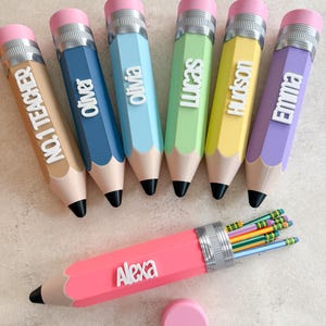 May include: A collection of seven large pencil-shaped containers in various pastel colours, each featuring a personalised name or title in white lettering. One pink container is open, revealing several standard yellow pencils inside.
