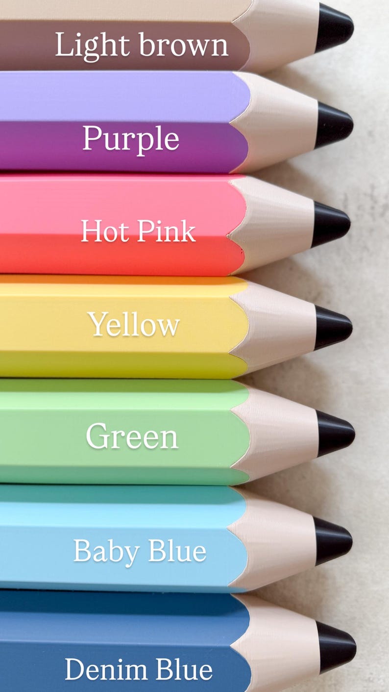 May include: A vertical stack of seven large pencil-shaped objects in light brown, purple, hot pink, yellow, green, baby blue, and denim blue. Each object features a tan wooden tip and a black lead point, with the colour name printed in white text.