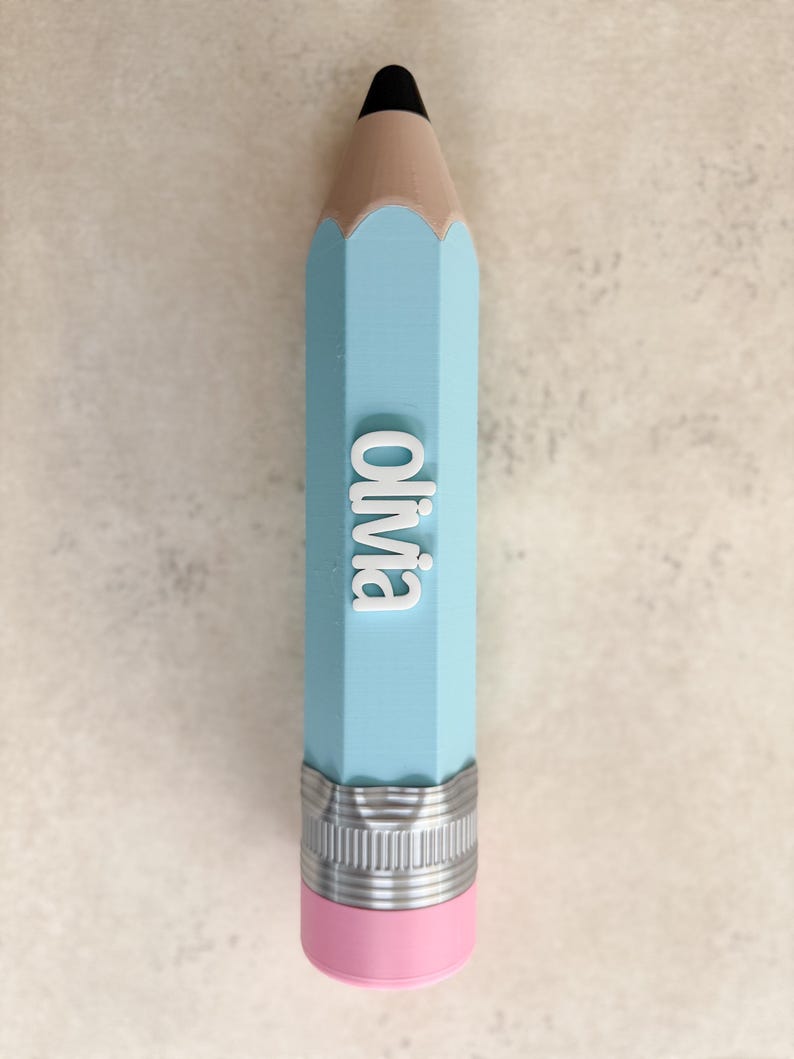 May include: A light blue pencil-shaped object featuring a black tip, a tan wooden-coloured section, and a silver-coloured metal ferrule above a pink eraser. The name Olivia is embossed in white, raised, sans-serif capital letters on the side.