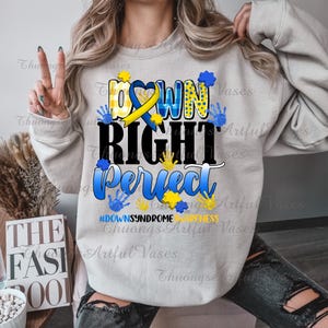 May include: Gray sweatshirt with the text "DOWN RIGHT PERFECT" in blue and yellow lettering. The text is surrounded by yellow and blue handprints. The text "#DOWNSYNDROME AWARENESS" is printed below the main text.