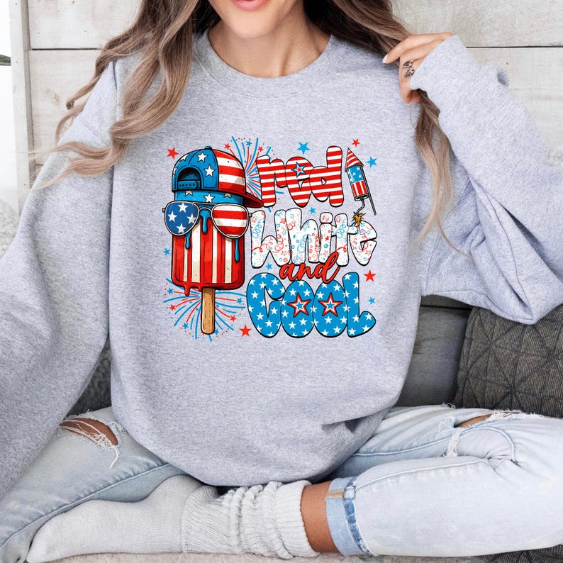 May include: A light gray sweatshirt with a patriotic design. The graphic features a popsicle wearing sunglasses and a baseball cap, with the words "Red, White, and Cool" in red, white, and blue.