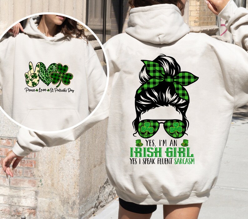 May include: A white hoodie with a green shamrock design and the text "Peace & Love & St Patrick's Day" on the front. The back of the hoodie features a cartoon illustration of a woman with a green plaid bun, sunglasses with shamrocks, and the text "YES, I'M AN IRISH GIRL YES I SPEAK FLUENT SARCASM".