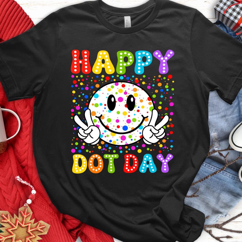 May include: Black t-shirt with a colorful graphic celebrating "Happy Dot Day." The design features a smiley face with peace signs, surrounded by dots, and the words "HAPPY DOT DAY" in rainbow colors.