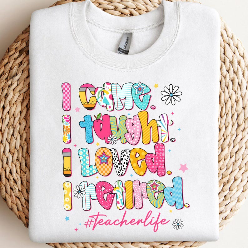May include: White sweatshirt with the text "I came, I taught, I loved, I retired" in colorful, patterned letters. The phrase "#Teacherlife" is also included. The design features stars, flowers, and a pencil.