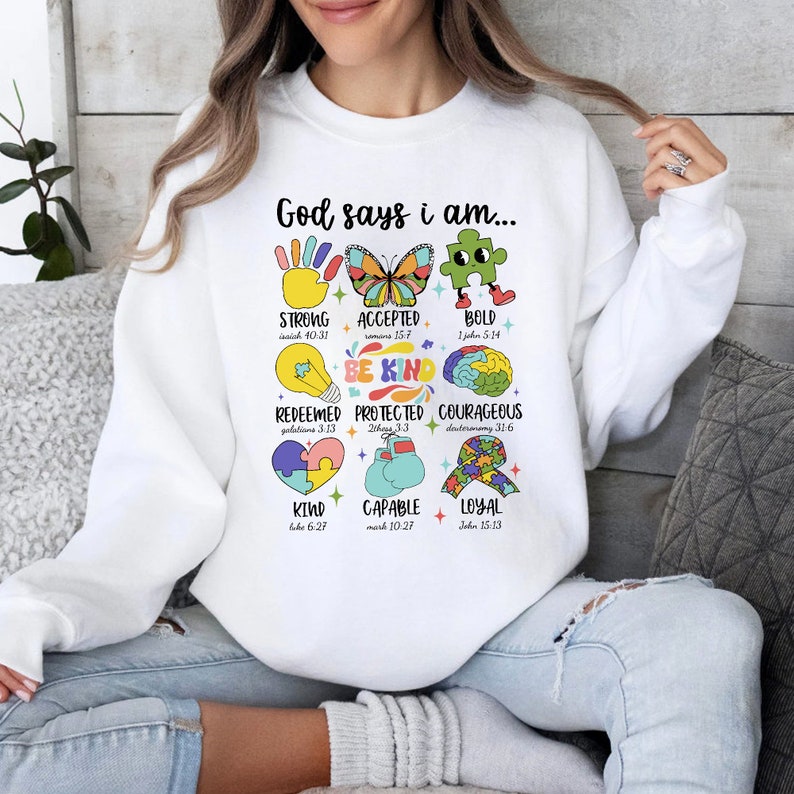 May include: White sweatshirt with a colorful graphic design that says "God says I am..." and lists positive attributes with bible verses. The graphic includes a hand, butterfly, puzzle piece, lightbulb, brain, heart, boxing glove, and a ribbon.