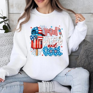 May include: White sweatshirt with a patriotic design featuring a popsicle wearing sunglasses and a baseball cap, with the text "Red, White, and Cool". The design incorporates red, white, and blue colors, fireworks, and stars.